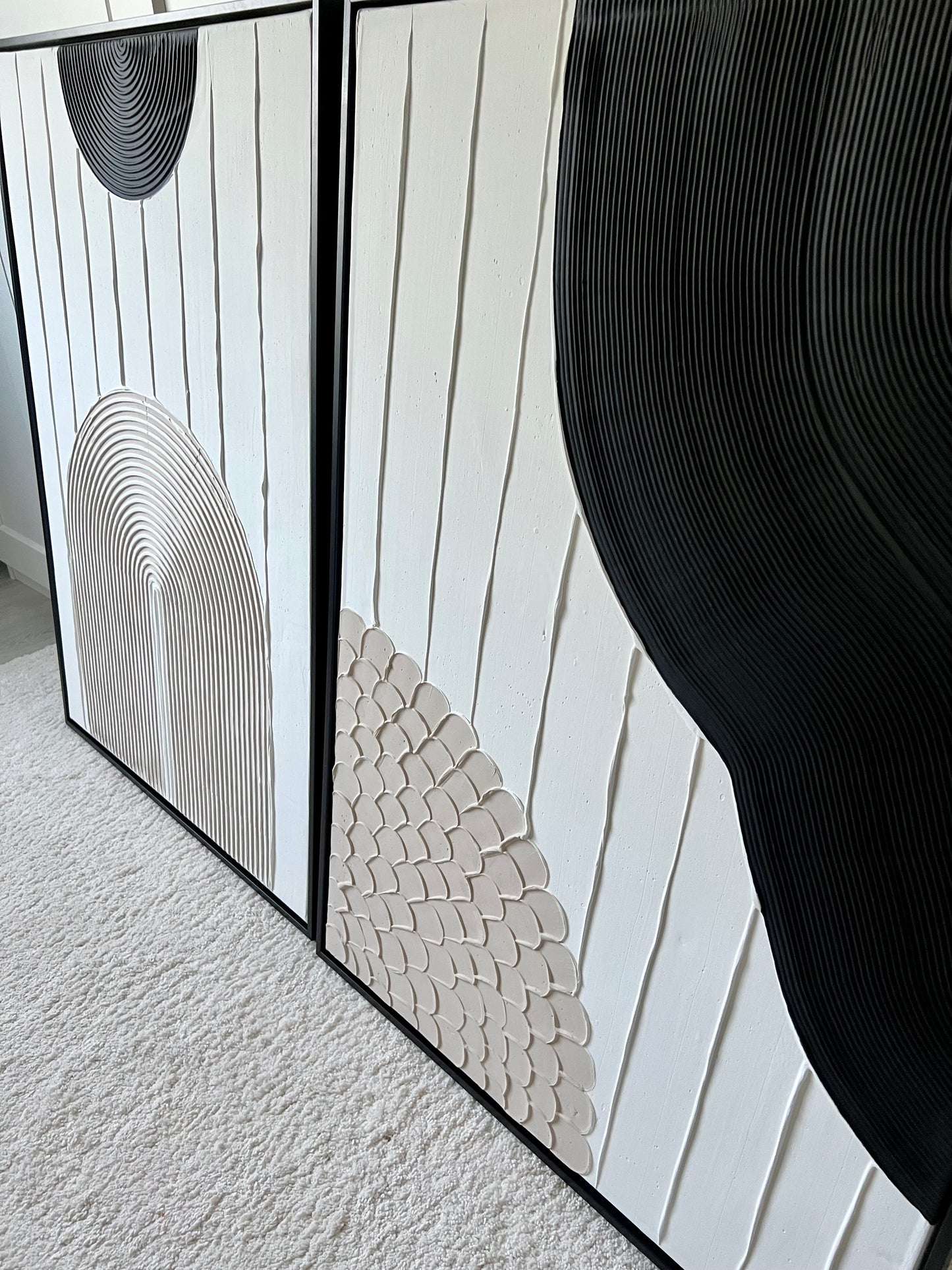 Decorative wall art with geometric patterns in black and white on a textured surface.