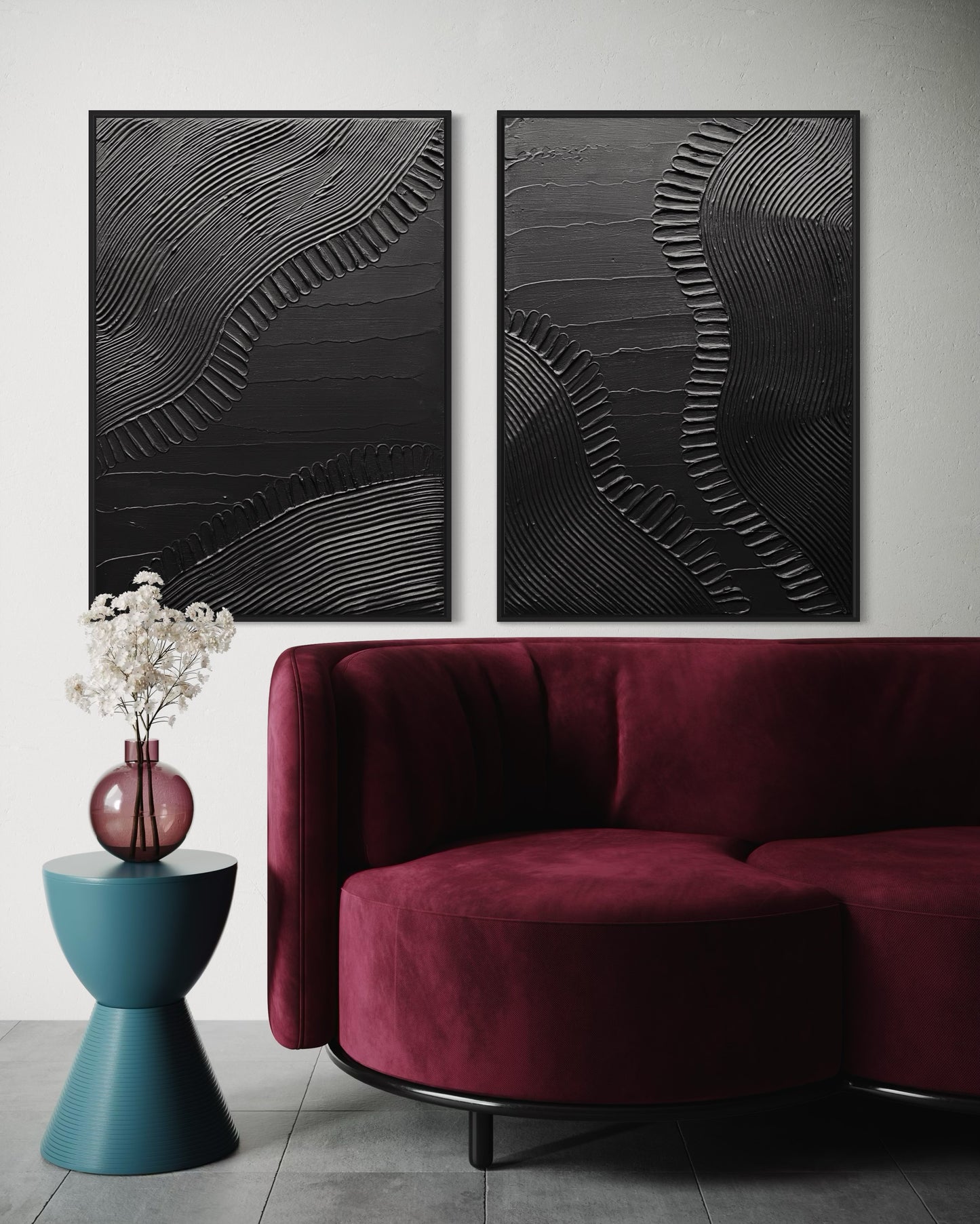Two abstract black artworks on a white wall above a burgundy sofa with a blue side table.