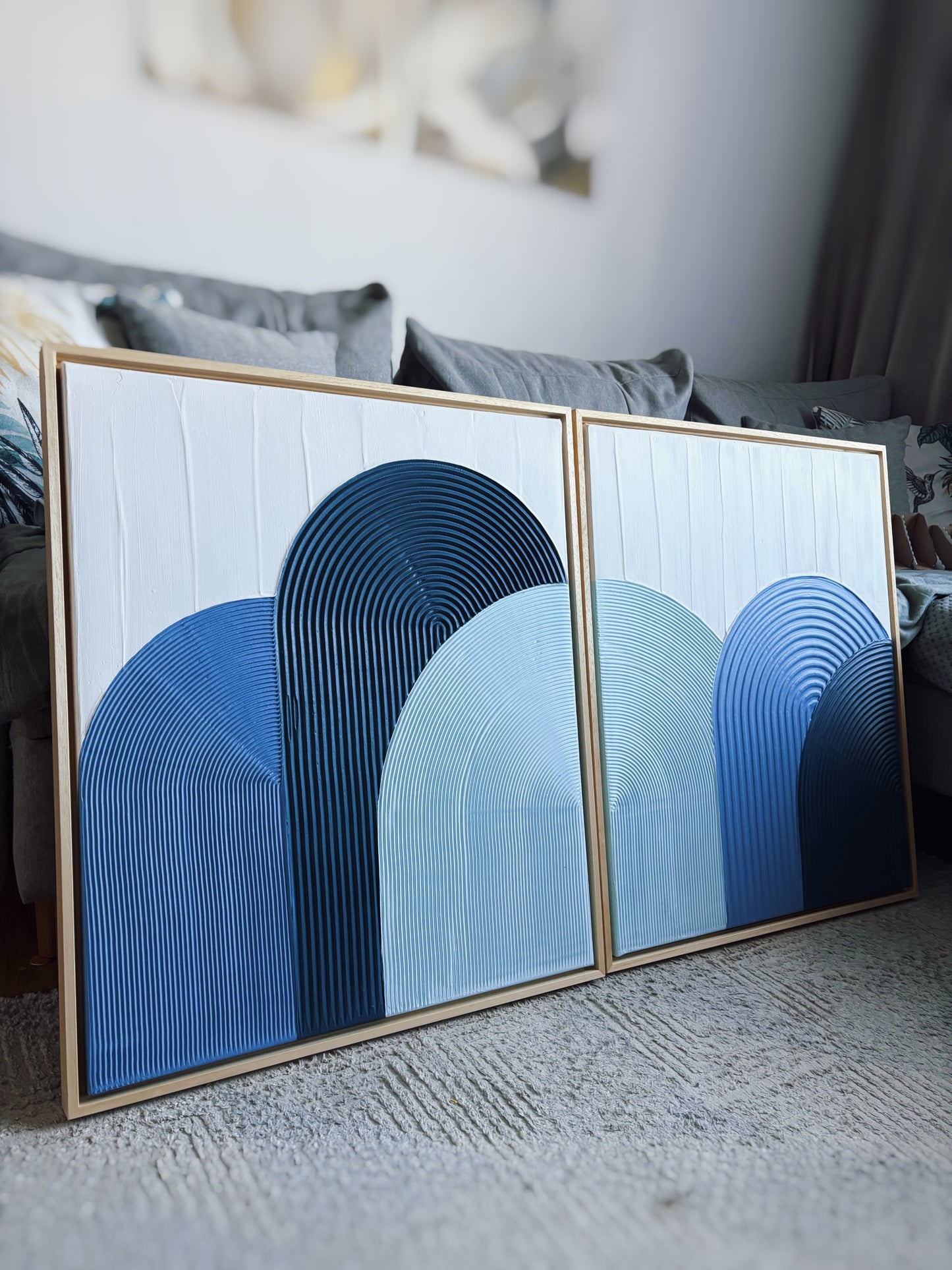 Two abstract art pieces with blue arches in a gold frame on a textured surface.