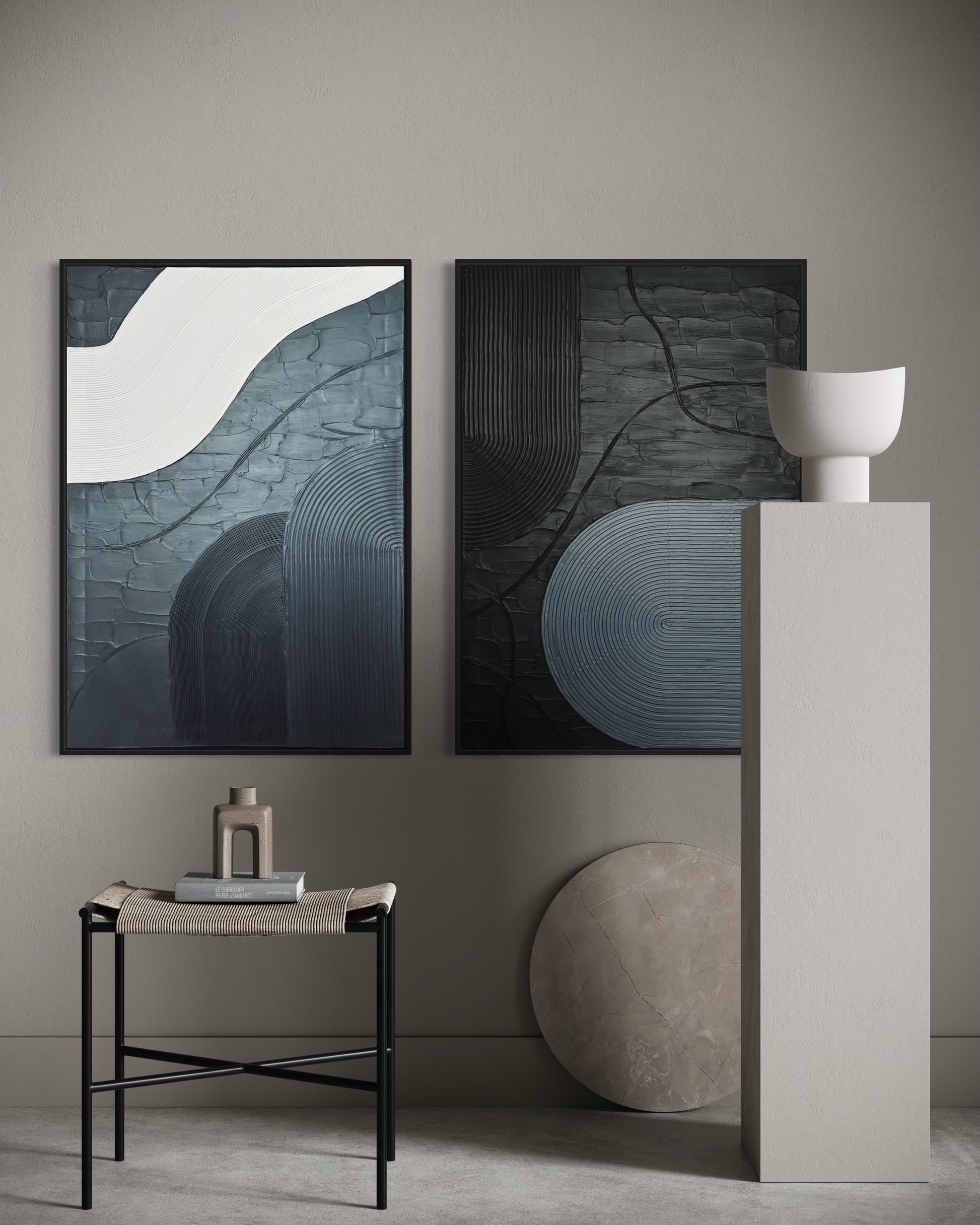 Two abstract artworks in grey and black, minimalist paintings on a wall with a side table and decorative items in a minimalistic setting.