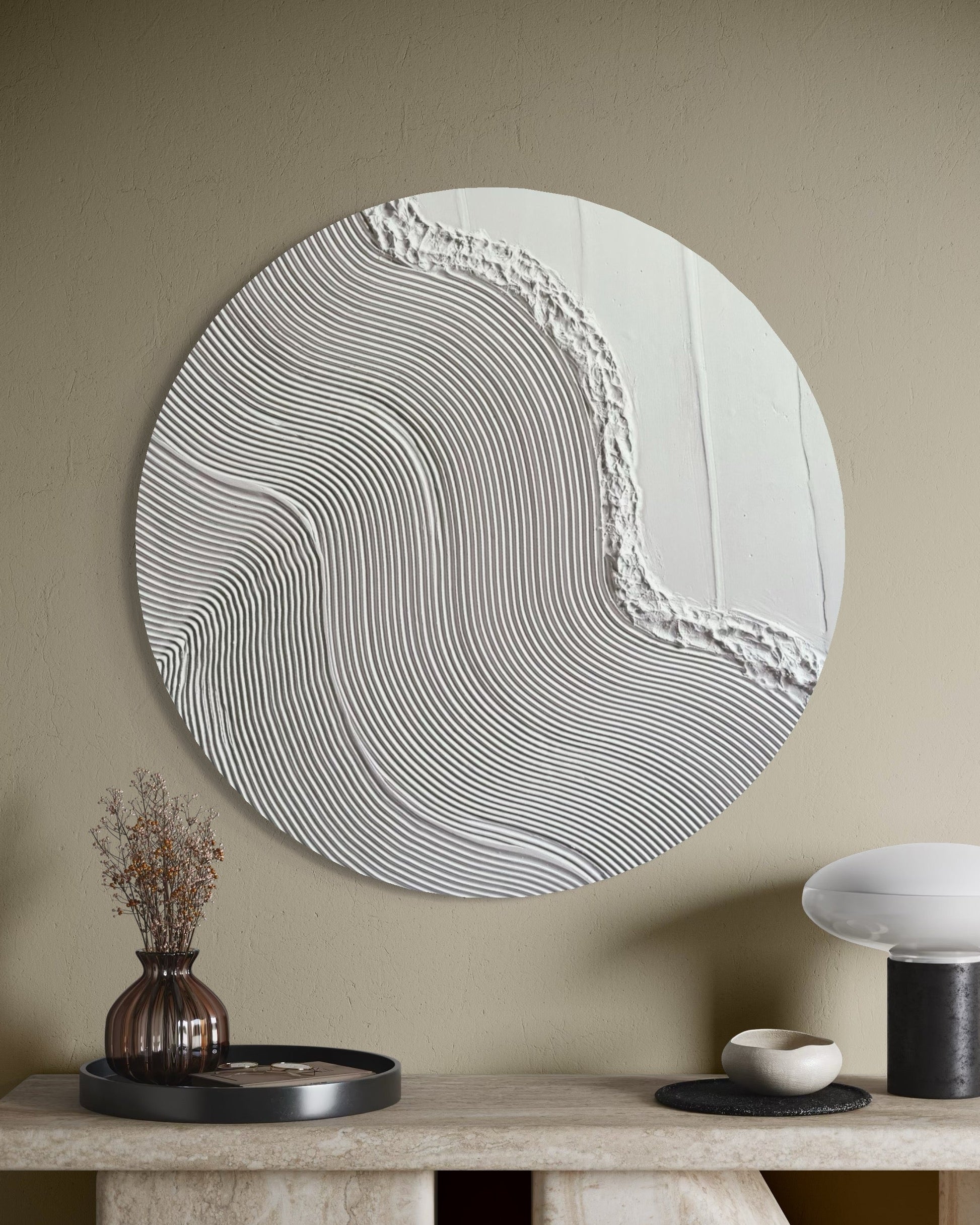 Round textured wall art on a beige wall above a console table with decorative items.
