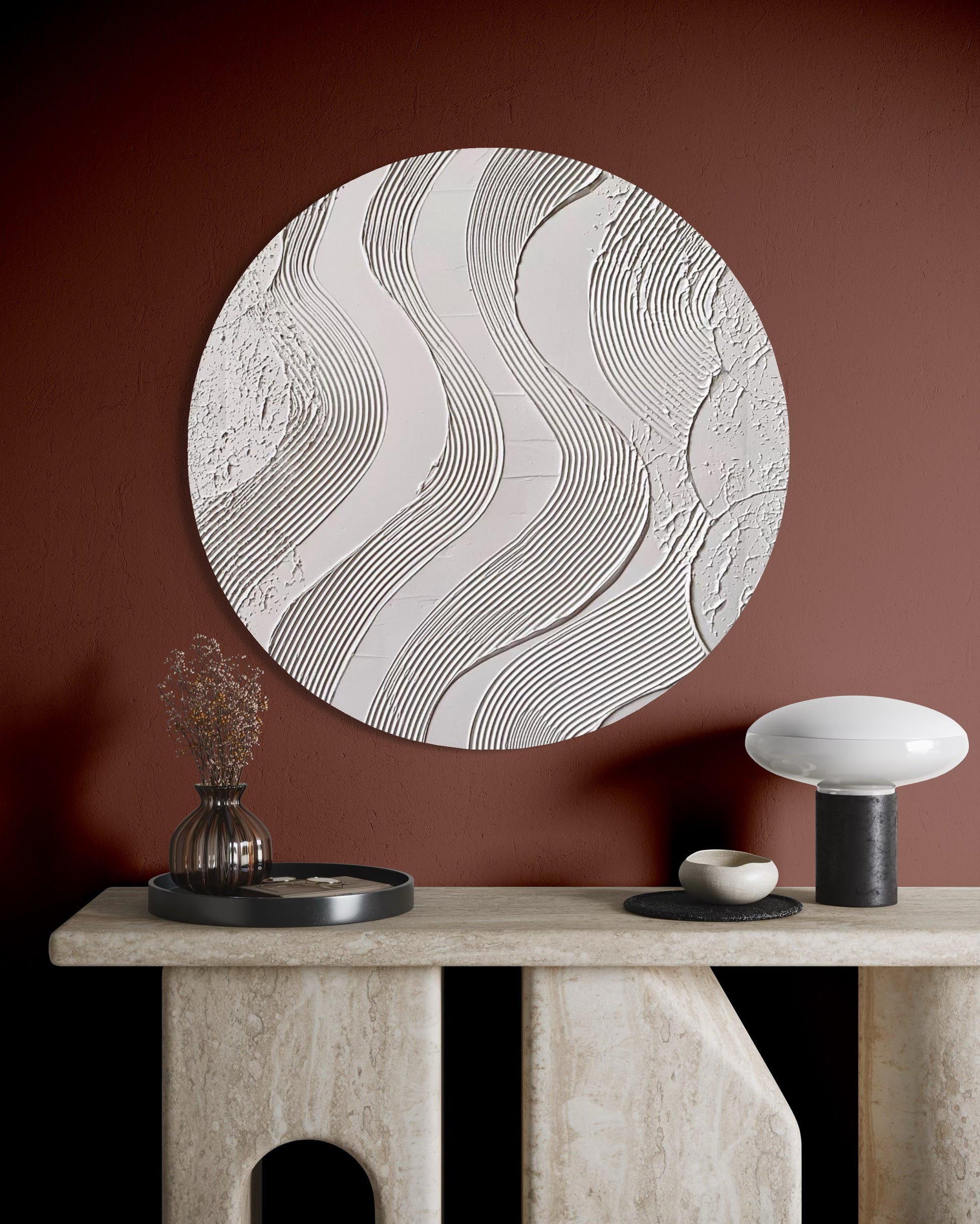 Round textured wall art piece on a brown wall with a stone console table and decorative items.