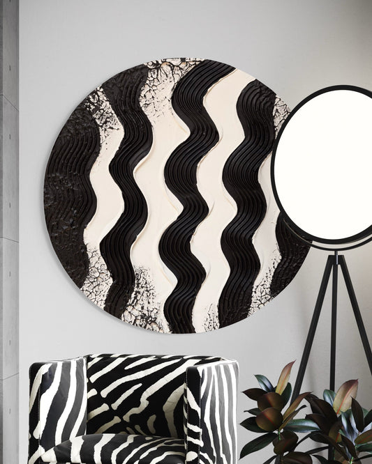 Round wall art with wavy black and white pattern on a gray wall, with a zebra-patterned chair and plant in the foreground.