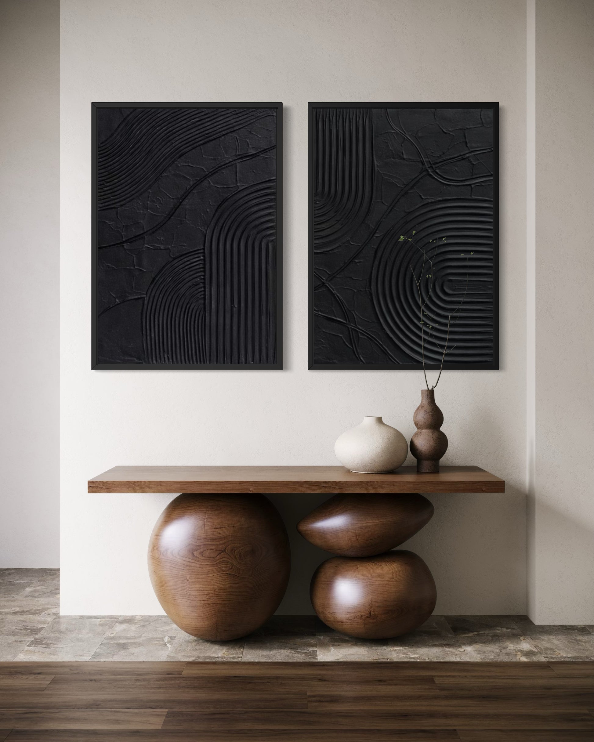 Two black abstract wall arts on a white wall with a wooden console table below.