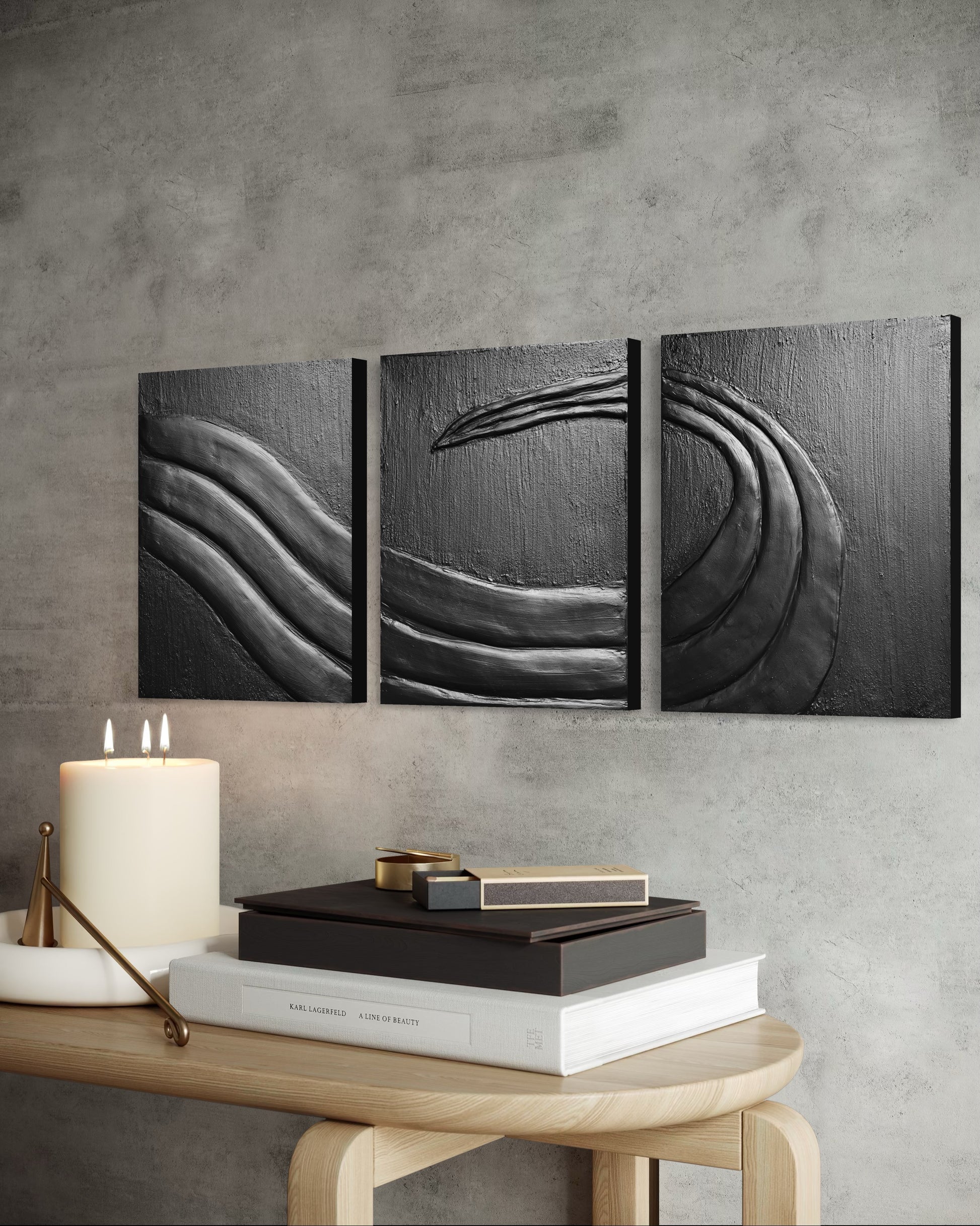 Three black and white abstract wall art pieces on a gray wall above a wooden table with decorative items.