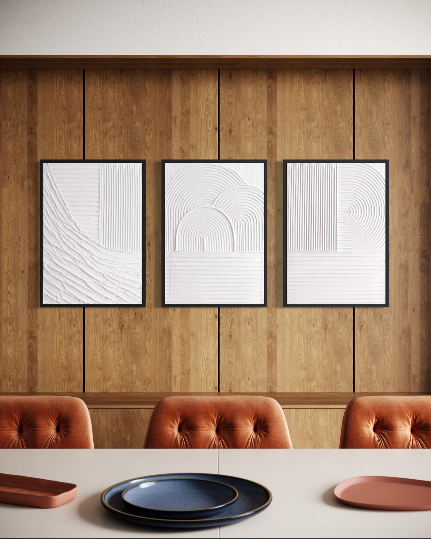 Three framed abstract artworks on a wooden wall above a dining table with plates.