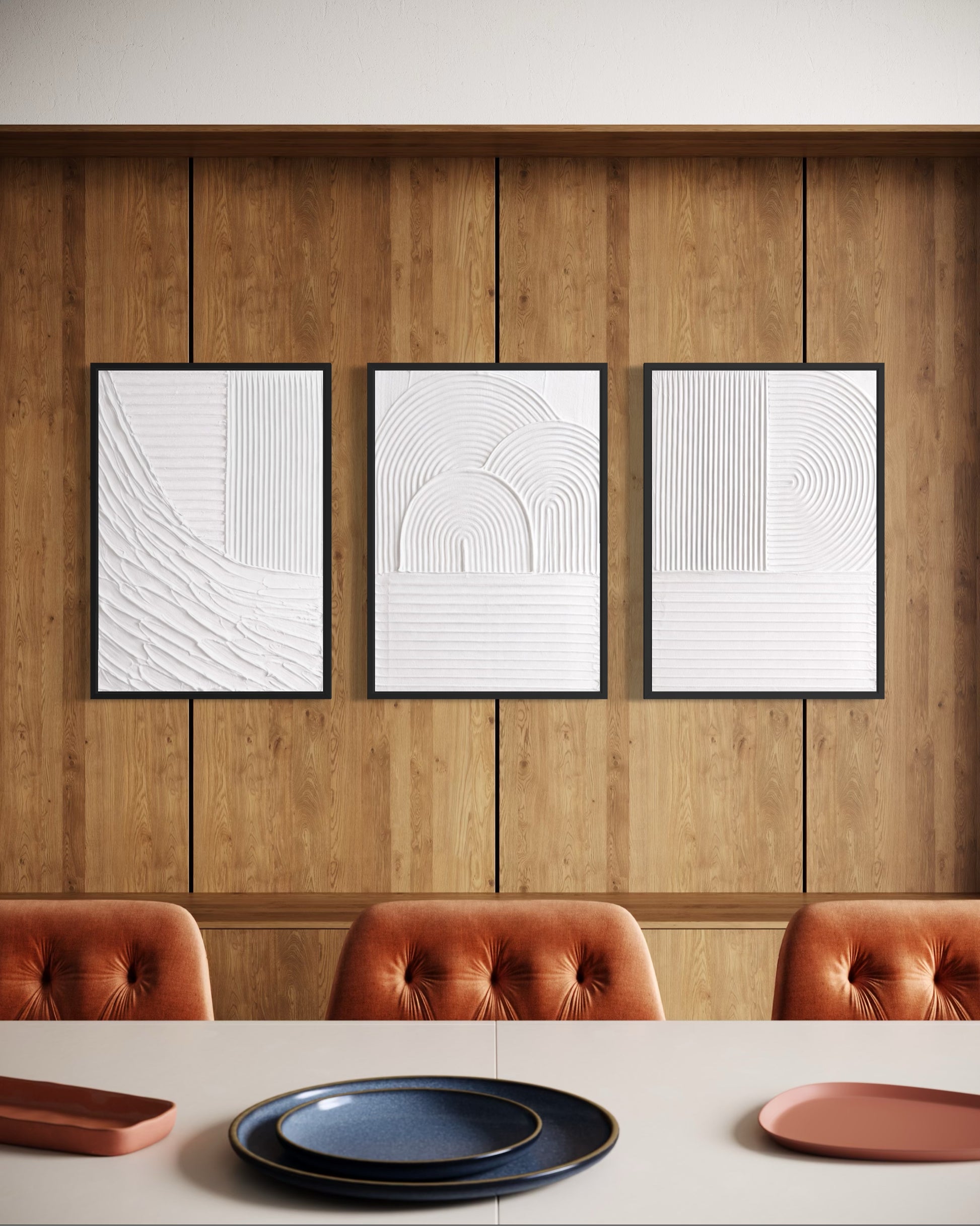 Three framed abstract artworks on a wooden wall above a dining table with plates.