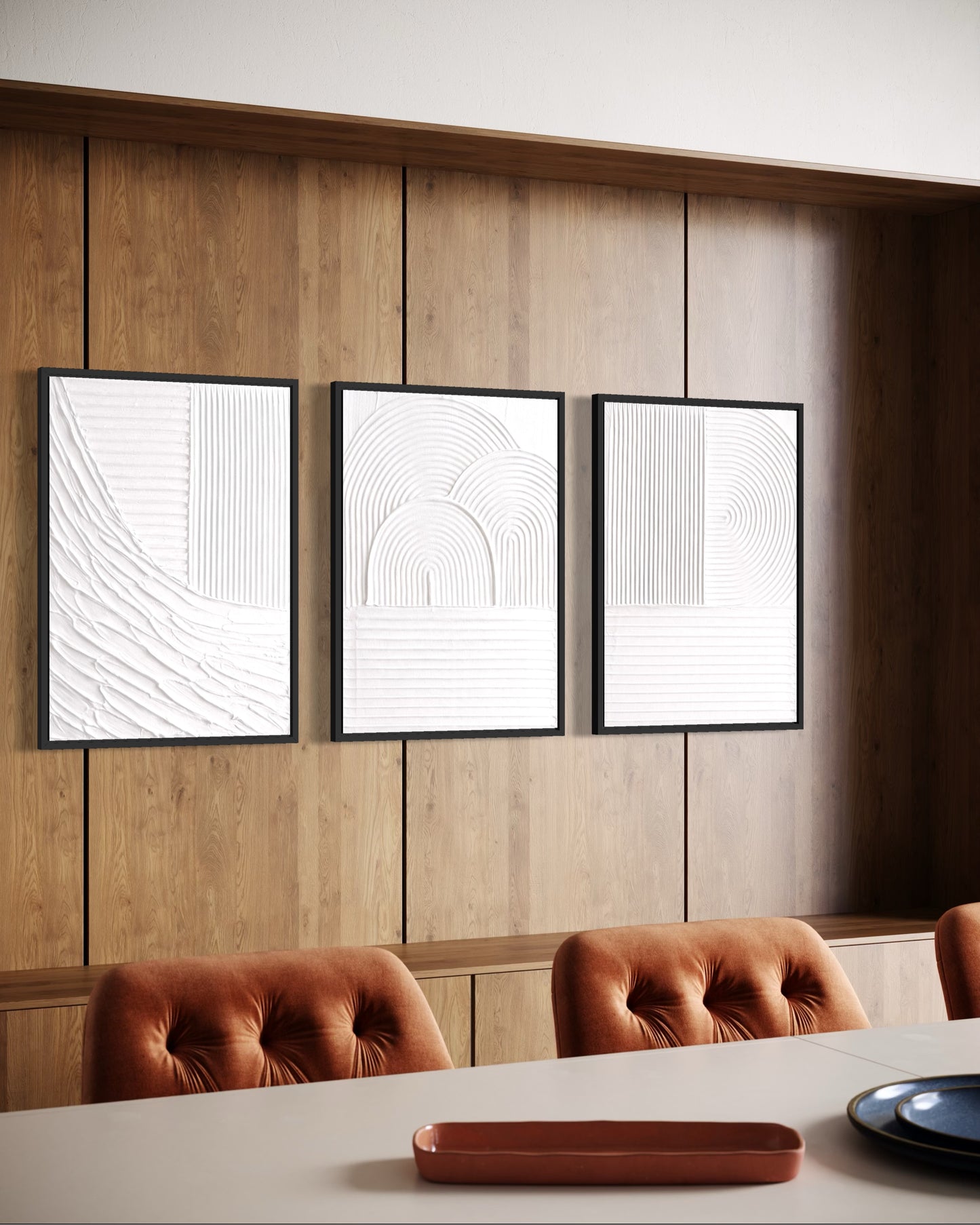 Three abstract art prints on a wooden wall above a dining table with chairs.
