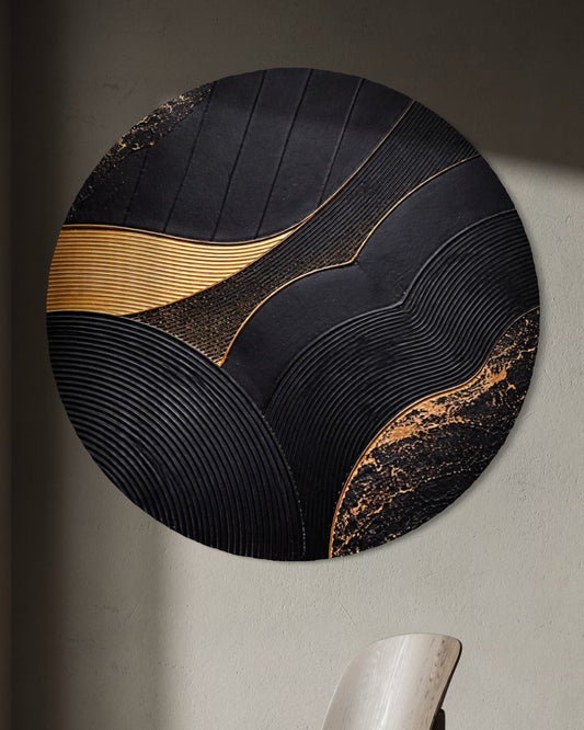 Round wall art piece with black and gold design in a room with a chair.