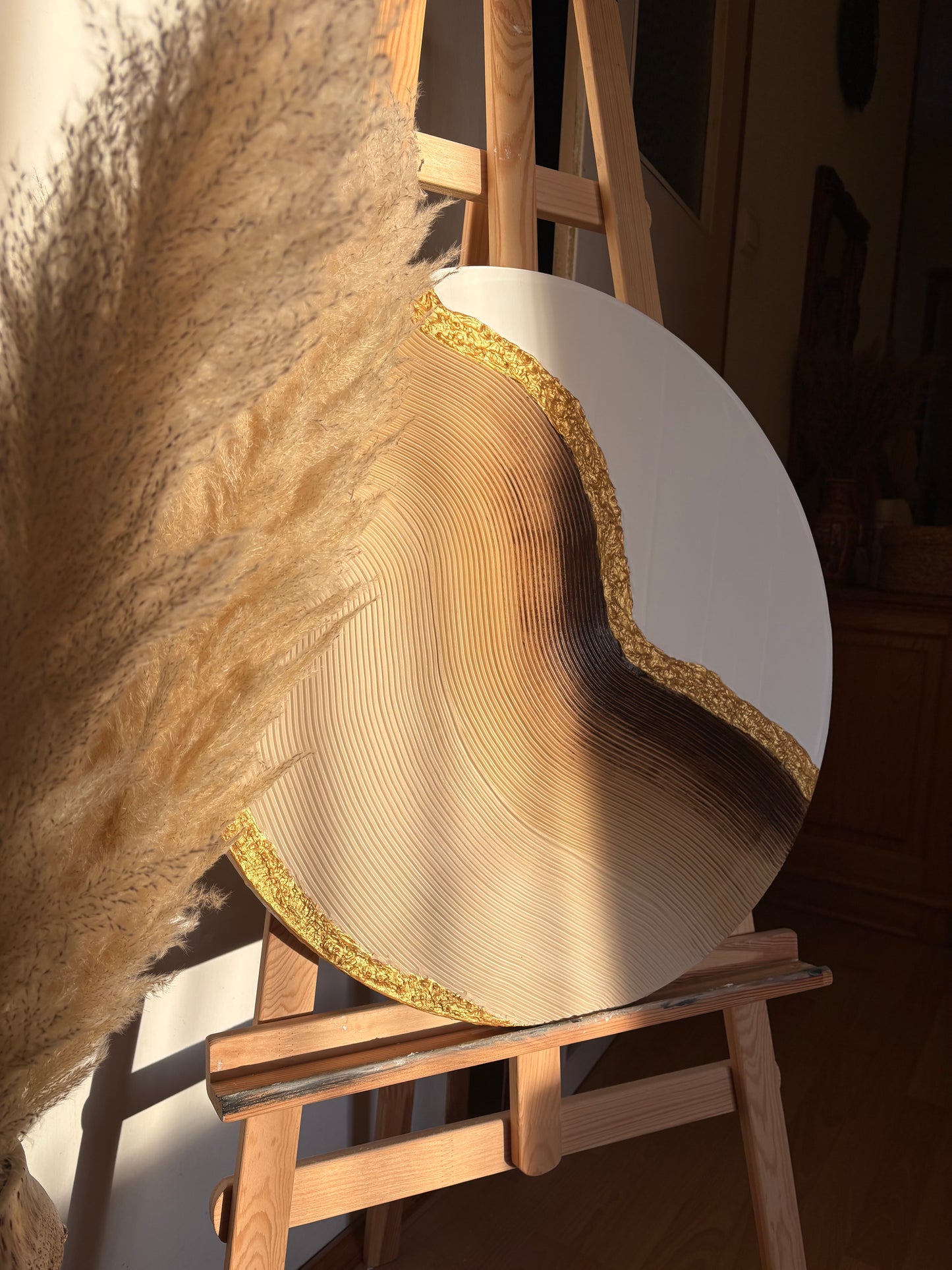 Wooden circular wall art with gold edge on a textured surface with pampas grass