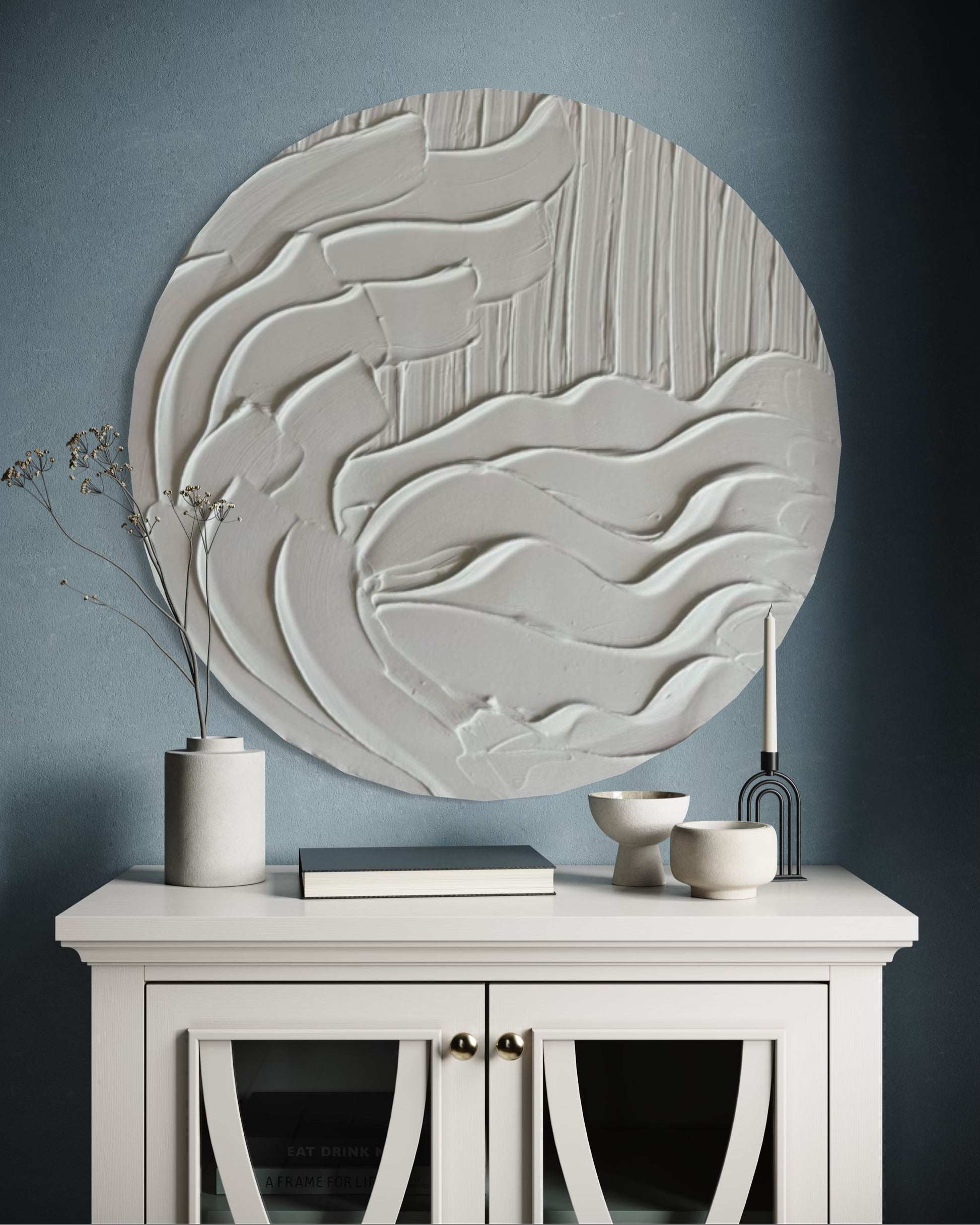 Decorative wall art piece on a gray wall above a white cabinet with decorative items.