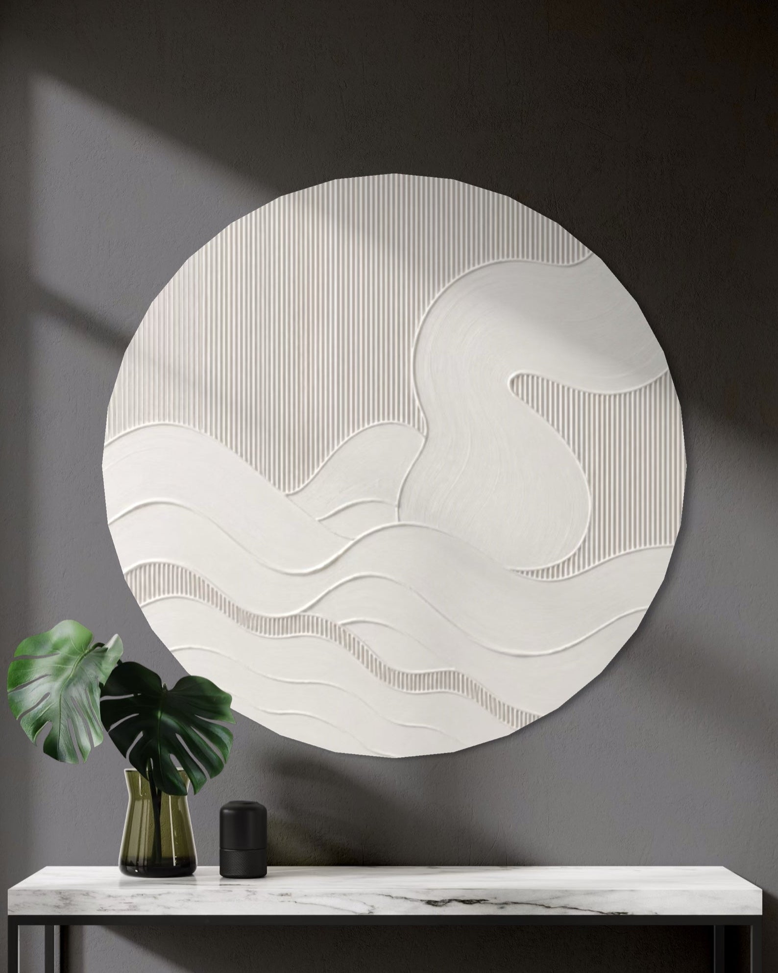 A large circular white textured wall art piece with wavy abstract lines hangs above a marble console table in a modern dark gray entryway. A green monstera leaf in a gold vase and a small black object sit on the table.