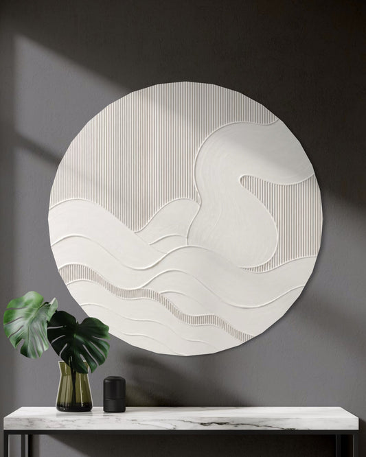 A large circular white textured wall art piece with wavy abstract lines hangs above a marble console table in a modern dark gray entryway. A green monstera leaf in a gold vase and a small black object sit on the table.
