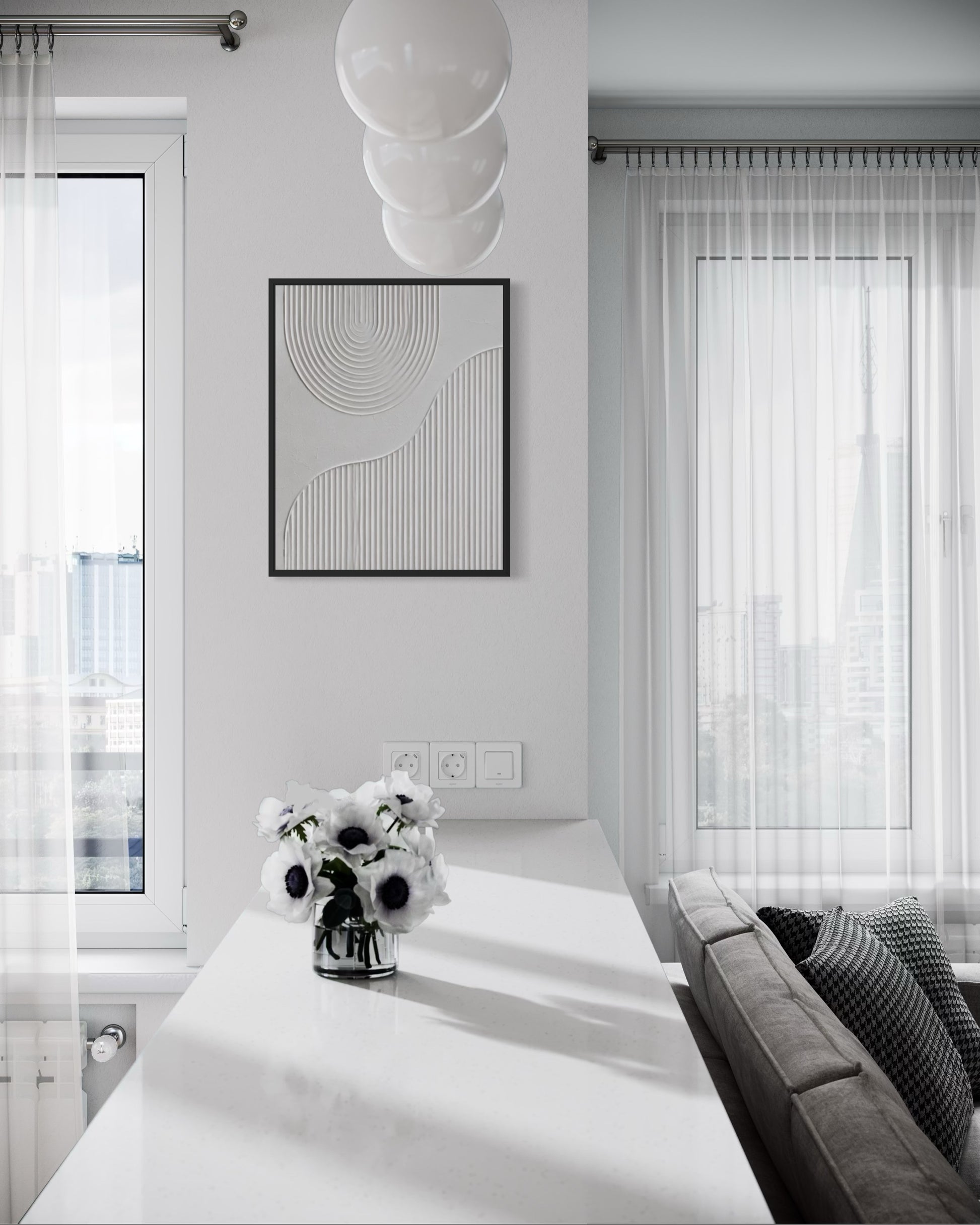A modern minimalist living room featuring a black-framed abstract line art print on a white wall above a white console table. The room has sheer white curtains, a gray sofa with patterned pillows, and a hanging cluster of three white globe pendant lights.