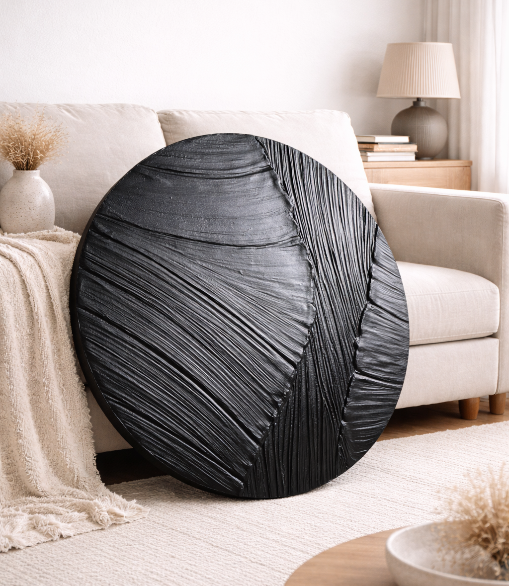 Round textured wall art in black with wavy texture on a couch in a living room setting