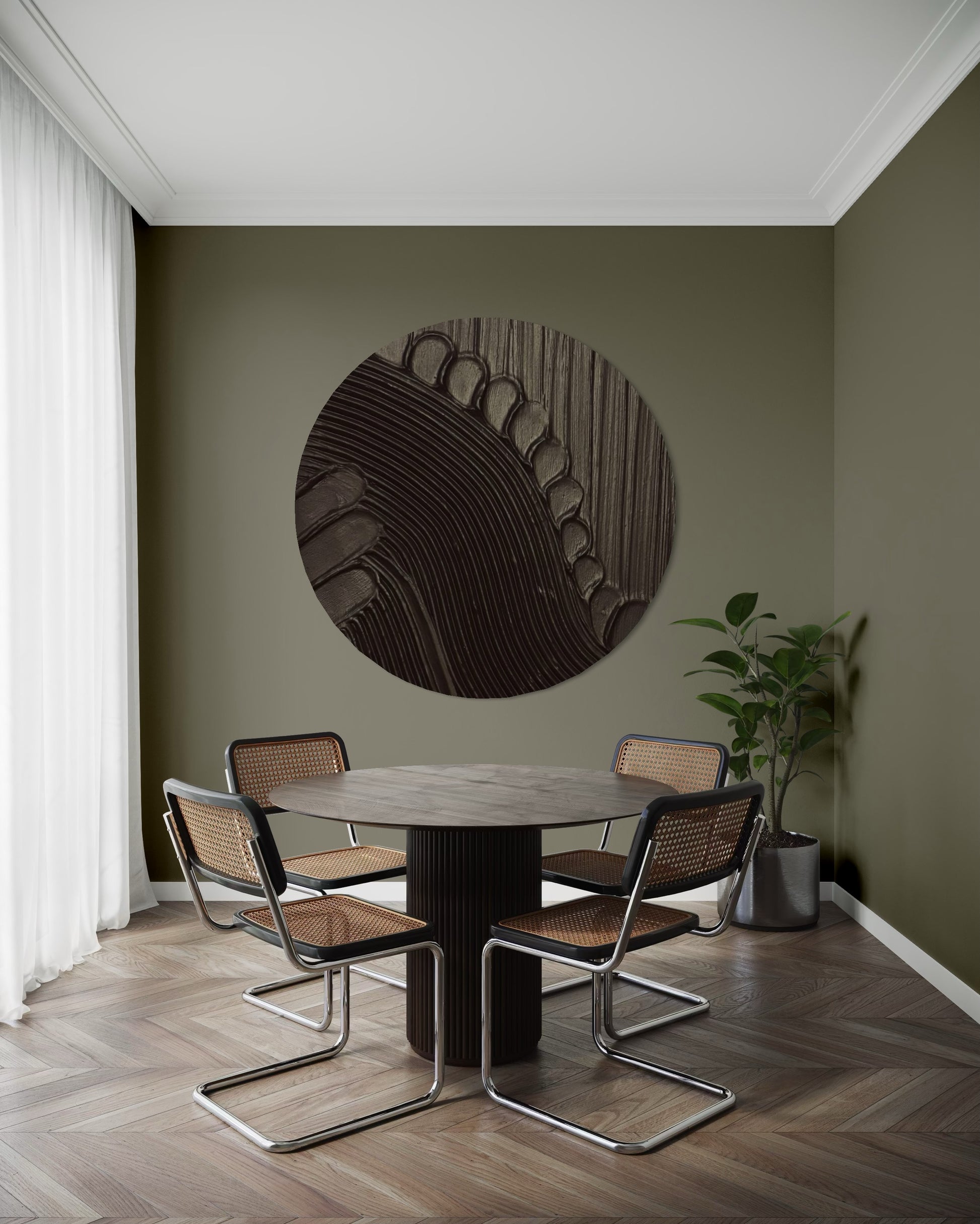 Dining area with a round table and chairs against a green wall with a decorative circular wall art piece.